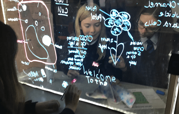 Two girls, both school students are working on a digital lightboard.