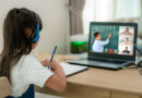 A little girl is learning online with the help of laptop and headphone besides, she has notebook to take notes and pen stand near to her.